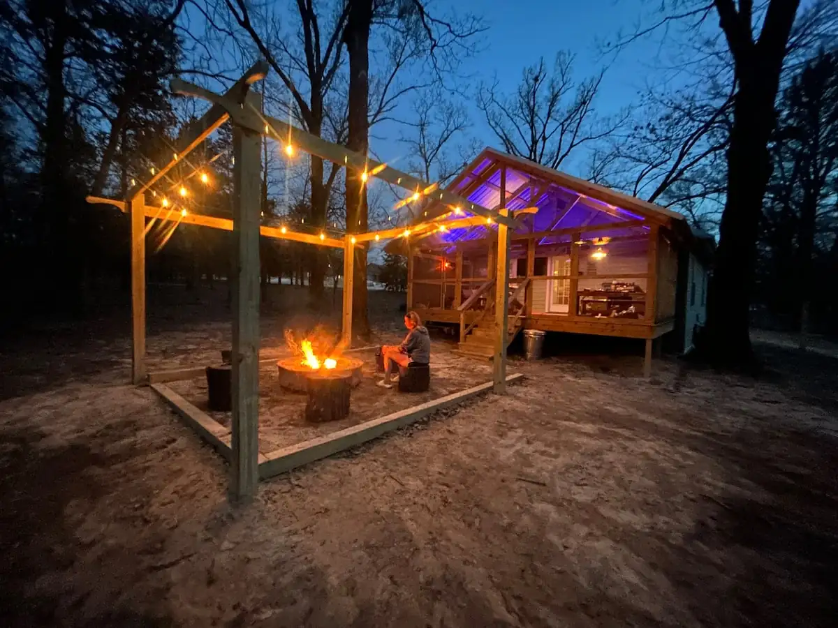 Fire pit burning under string lights beside the cabin porch at night